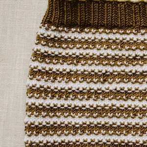 May include: A close-up of a knitted fabric with horizontal stripes in brown and white.