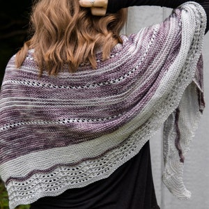 May include: A purple and white knitted shawl with a lacy border. The shawl is draped over a person's shoulders.