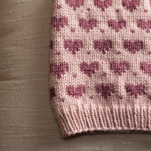 May include: A pink knitted headband with a repeating pattern of small pink hearts.