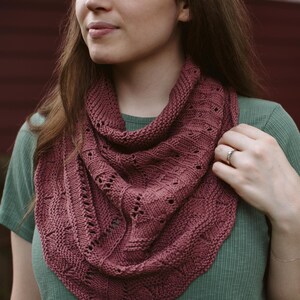 May include: A close-up of a woman wearing a mauve knitted shawl with a delicate lace pattern. The shawl is draped around her neck and shoulders, and she is wearing a green shirt.