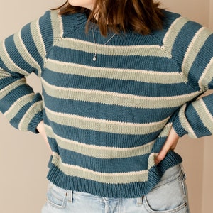 May include: A blue and green striped sweater with long sleeves. The sweater has a relaxed fit and a round neckline.