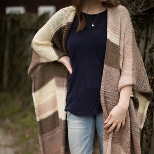 May include: A brown, beige, and white striped knitted cardigan with a long, open front. The cardigan is worn over a dark blue t-shirt and blue jeans.