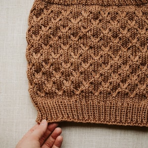 Puede incluir: Un gorro de punto marrón con un patrón de rombos.