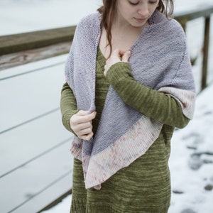 Puede incluir: Una mujer con un suéter verde y una chal de punto morado y blanco. La chal tiene un borde colorido.