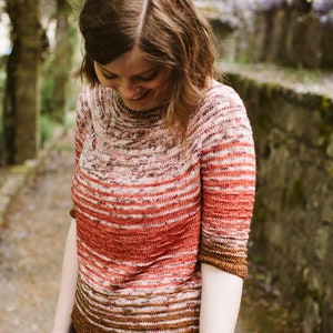 Puede incluir: Una mujer lleva un suéter a rayas de color óxido con un patrón marrón y blanco. El suéter tiene un corte holgado y una longitud ligeramente recortada.