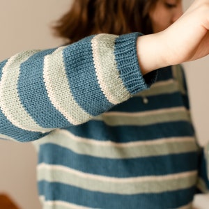 May include: A blue and white striped jumper with long sleeves. The jumper is made of a soft, knitted fabric.