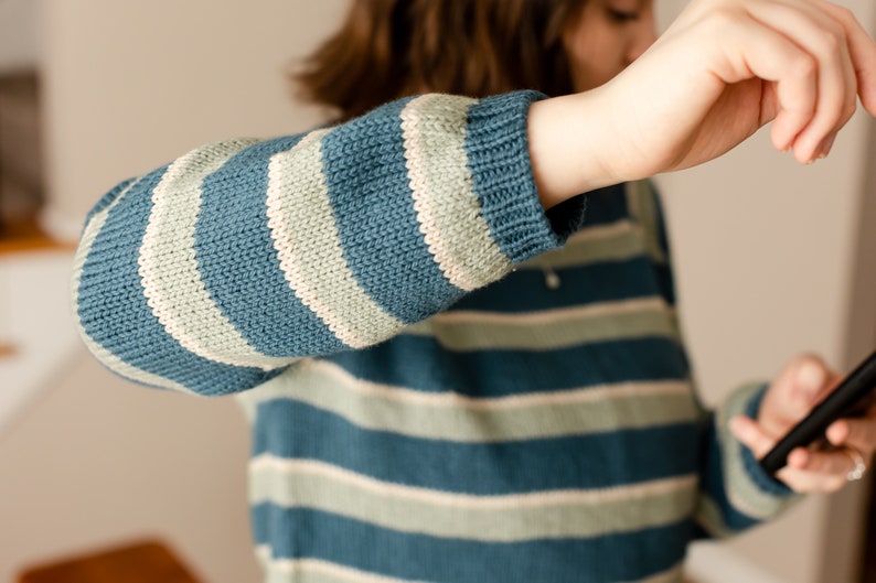 May include: A blue and white striped jumper with long sleeves. The jumper is made of a soft, knitted fabric.