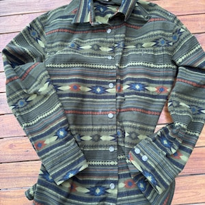 May include: A button-down shirt with a Southwestern-inspired pattern. The shirt features a mix of olive green, blue, red, and cream colors in a geometric design. It has long sleeves and a collared neckline.