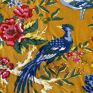 May include: Mustard yellow fabric with a floral and bird pattern. The design features blue birds, red and pink roses, and blue and pink flowers with green leaves. The birds are perched on white branches.