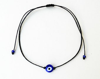 Könnte beinhalten: Ein schwarzes Armband aus Schnur mit einem blauen Glücksbringer in Form eines bösen Auges. Der Glücksbringer hat eine weiße Mitte.