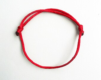 Puede incluir: Un brazalete de cuerda roja con dos nudos en los extremos.