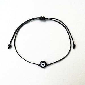 May include: A black string bracelet with a small black and white evil eye charm.