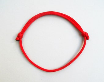 Könnte beinhalten: Ein leuchtend rotes Armband aus geflochtenem Kordel, an beiden Enden mit Knoten versehen. Das kreisförmige Armband liegt vor einem weißen Hintergrund. Die Kordel hat einen Durchmesser von etwa 0,6 cm.