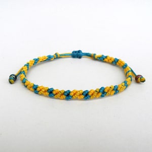 Puede incluir: Un brazalete de amistad trenzado amarillo y azul con cierre de nudo.
