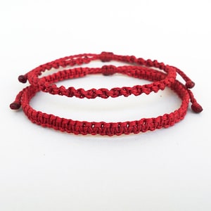 Peut inclure: Deux bracelets tressés rouges, l'un sur l'autre, sur un fond blanc.