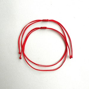 Puede incluir: Dos pulseras de cuerda roja atadas juntas en un círculo.