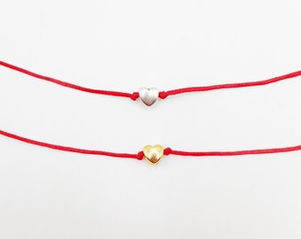 Könnte beinhalten: Zwei rote Armbänder mit Herzanhängern. Ein Anhänger ist silber und der andere ist gold.