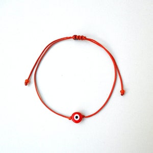 Puede incluir: Pulsera de cuerda roja con un amuleto de ojo azul.