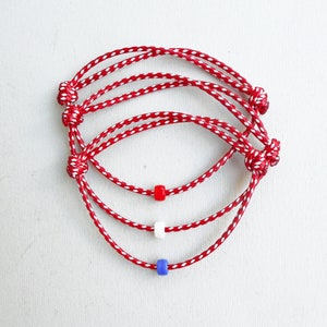 Könnte beinhalten: Drei rot-weiß gestreifte Armbänder mit roten, weißen und blauen Perlen.