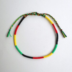 May include: A braided friendship bracelet with red, yellow, green, and black threads. The bracelet is tied in a knot at the end.