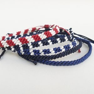 May include: A set of four friendship bracelets in red, white, and blue colors. The bracelets are made of braided string and have a simple design.