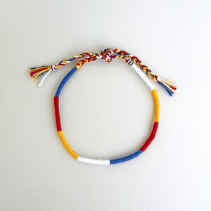 May include: A colorful friendship bracelet with red, yellow, blue, and white threads woven together in a circular pattern.