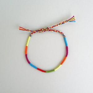 May include: A colorful braided friendship bracelet with red, orange, yellow, green, blue, and purple threads.