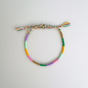 Op de afbeelding: Een kleurrijk vriendschapsarmbandje met groene, gele, roze, paarse en bruine draden.