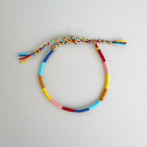 Könnte beinhalten: Ein farbenfrohes Freundschaftsarmband aus geflochtenen Fäden in Blautönen, Gelb, Rot und Rosa.