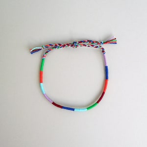 May include: A colorful braided friendship bracelet with red, orange, yellow, green, blue, purple, and white threads.