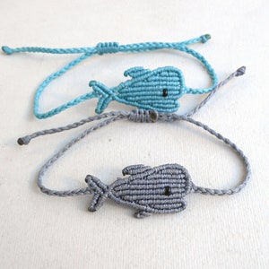 Può includere: Due braccialetti dell'amicizia con un design a pesce annodato. Un braccialetto è azzurro chiaro e l'altro è grigio.