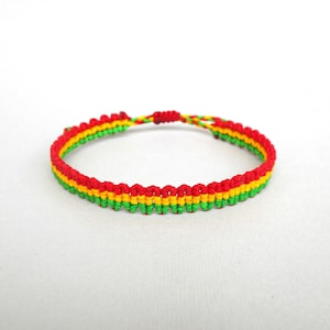 Może przedstawiać: Bransoletka przyjaźni w kolorze czerwonym, żółtym i zielonym, wykonana z plecionego sznurka.