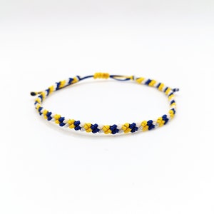 May include: A blue, white, and yellow friendship bracelet with a braided design.