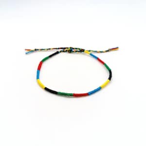 Puede incluir: Un brazalete de amistad colorido con hilos negros, amarillos, rojos, azules y verdes.