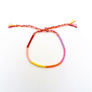 May include: A multi-colored friendship bracelet with pink, red, orange, and yellow threads.