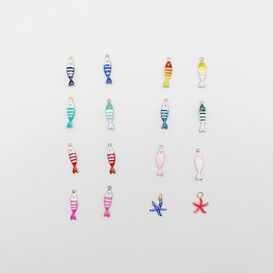 Könnte beinhalten: Eine Sammlung von sechzehn kleinen Metallanhängern mit Emaille-Motiven von Fischen und Seesternen in verschiedenen Farben wie Blau, Rot, Gelb, Grün, Rosa und Weiß. Jeder Anhänger verfügt über eine kleine Öse an der Oberseite zur Befestigung.