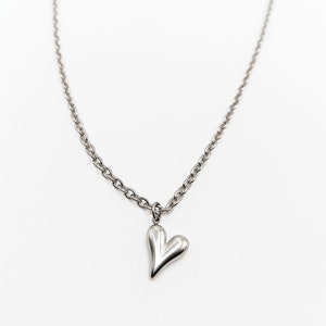 Puede incluir: Un collar de cadena de plata con un pequeño colgante de corazón de plata.