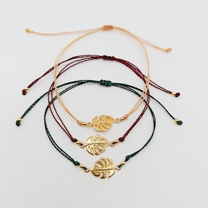 May include: Three adjustable bracelets with gold leaf charms. The bracelets are made of thin cord in green, burgundy, and beige.