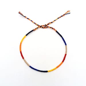 May include: A colorful friendship bracelet with blue, orange, yellow, and beige threads woven together.