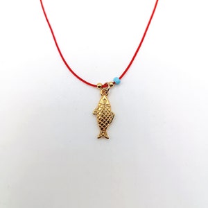 May include: A gold fish charm necklace with a red string and blue beads.