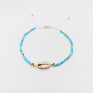 May include: A turquoise beaded bracelet with a natural seashell centrepiece. The bracelet features small gold-coloured beads interspersed with the turquoise beads. The adjustable white cord allows for a comfortable fit. This beach-themed jewellery is perfect for summer.