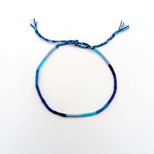 Könnte beinhalten: Ein blaues und hellblaues Freundschaftsarmband aus geflochtener Schnur.