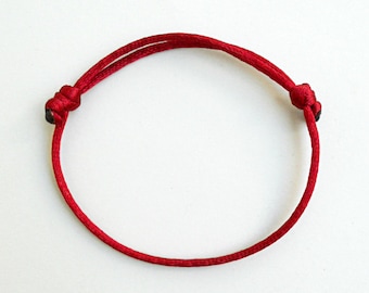 Puede incluir: Un brazalete de cuerda roja con dos nudos en los extremos.
