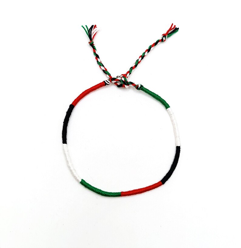 May include: A green, white, black, and red braided friendship bracelet. The bracelet is tied in a knot at the end.