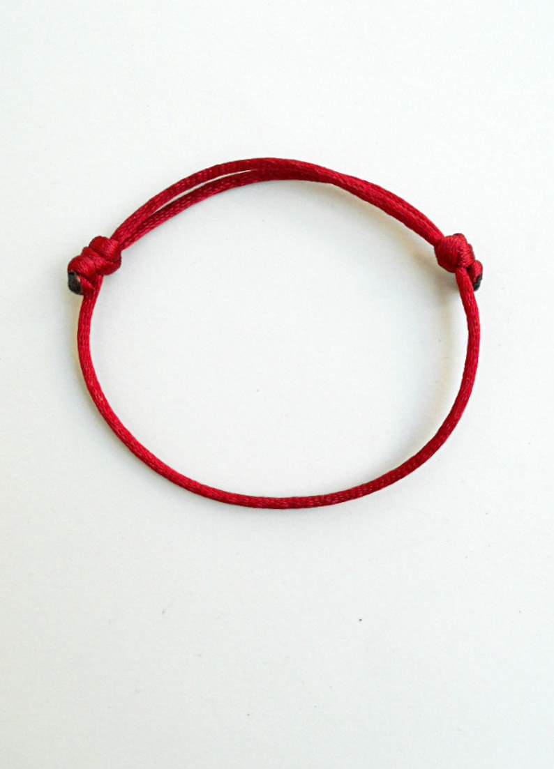 K&ouml;nnte beinhalten: Ein rotes Armband aus Schnur mit zwei Knoten an den Enden.
