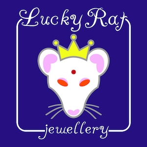 Op de afbeelding: Een grafisch logo op een donkerblauwe achtergrond met een witte rattenkop met roze oren, oranje ogen en een rode stip op het voorhoofd. De rat draagt een gele kroon met kleine gele cirkels. De tekst Lucky Rat jewellery is in het wit.