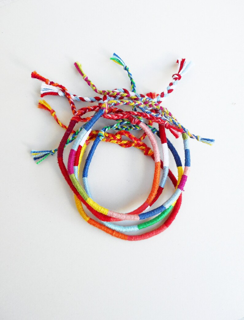 May include: A set of colorful friendship bracelets made with woven thread. The bracelets are in shades of red, blue, green, yellow, and white.