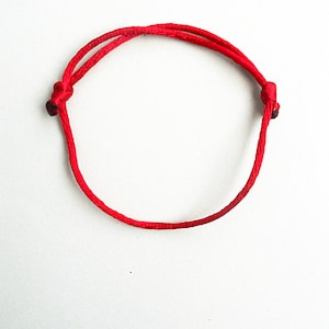 May include: A red string bracelet with a simple knot design.