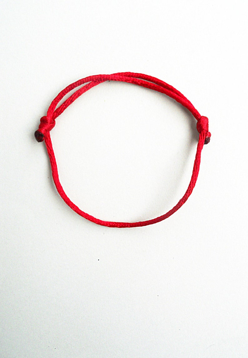 May include: A red string bracelet with a simple knot design.