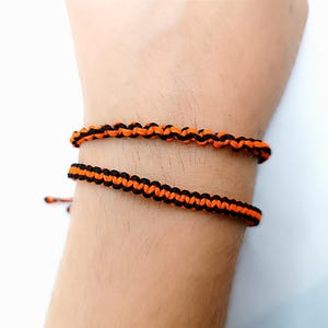 May include: A black and orange braided bracelet on a person's wrist.